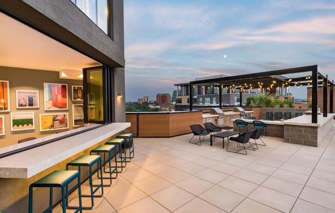 Rooftop lounge with bar seating, grill stations, and shaded spaces for casual hangs or evening gatherings under the string lights.