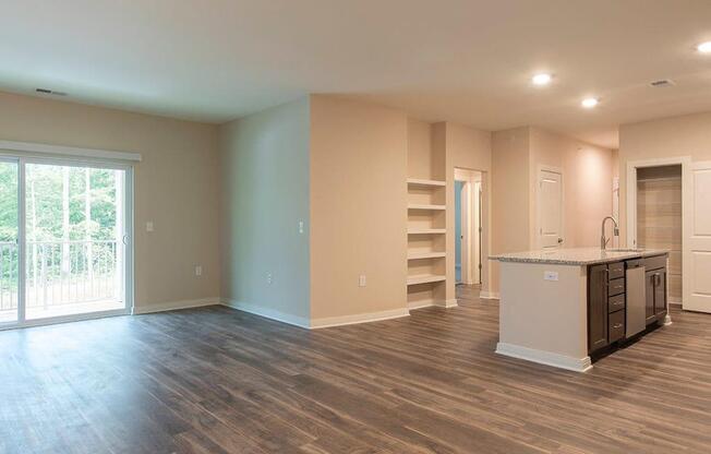 an empty living room with a kitchen and a door leading to a balcony  at Sapphire at Centerpointe, Midlothian, VA