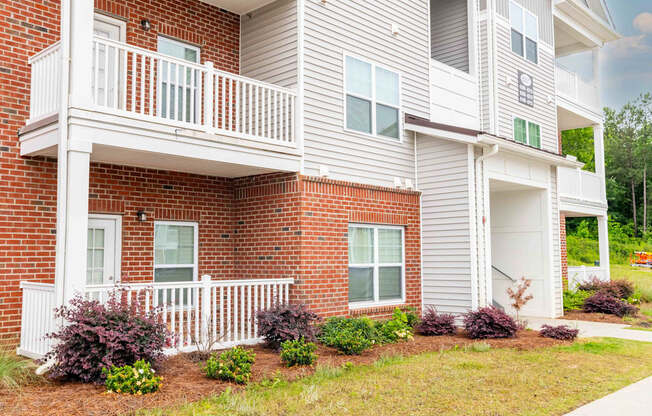 A two-story apartment building with a balcony and a small garden in front.