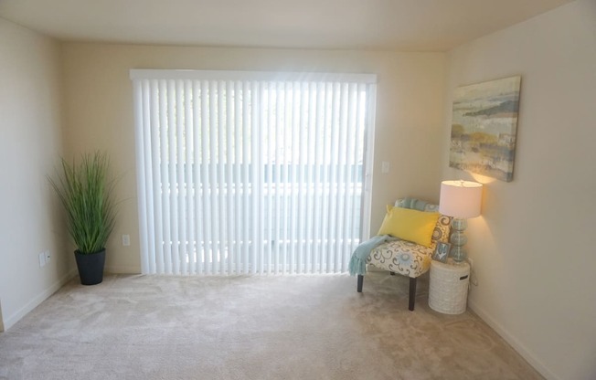 a living room with a large sliding glass door, beige carpet and a chair at Heritage Grove Apartments in Renton, WA