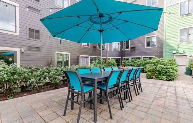 A blue umbrella is over a table with chairs on a patio.