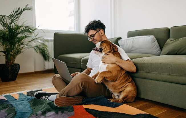 a man sitting on the floor with his dog and laptop