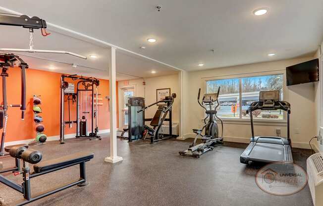 A fitness center with a wall of mirror and an orange accent wall, featuring weight training equipment and cardio equipment.