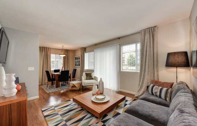 Dining Area and Living Room with Wood Inspired Floors,  Gray Sofa, Short Wood Table, Open Window Blinds, Lamp, Dining Room Table and Chairs