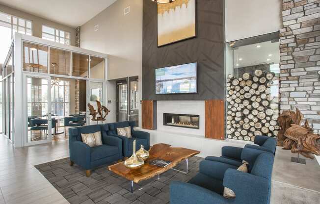 Lobby lounge area with blue armchairs, fireplace with logs and television mounted overhead