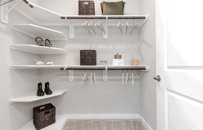 a walk in closet with white shelves and hooks and a white closet door with shoes