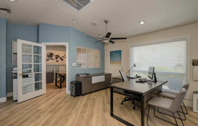 The Legacy Leasing office with large desk and chairs for meeting with prospective renters.  Office has light colored wood flooring and a light blue accent wall.