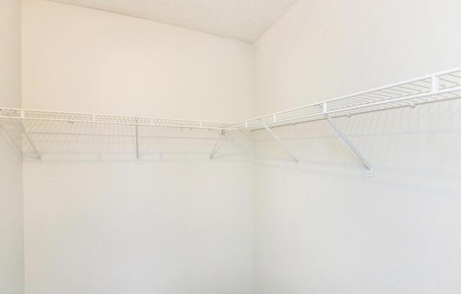Empty room corner featuring white wire shelving mounted on a light-colored wall. The shelves are designed for organization, with no items displayed on them, creating a minimalistic and clean appearance.
