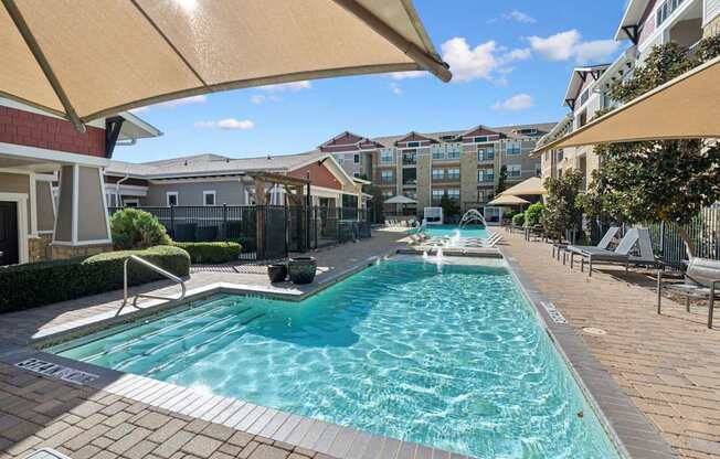 A swimming pool surrounded by a patio and apartment buildings.