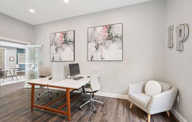 A room with a desk, chairs, and a couch with a painting on the wall.