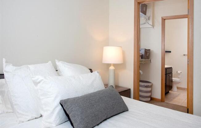 A bed with white pillows and a grey pillowcase with a lamp on the side.