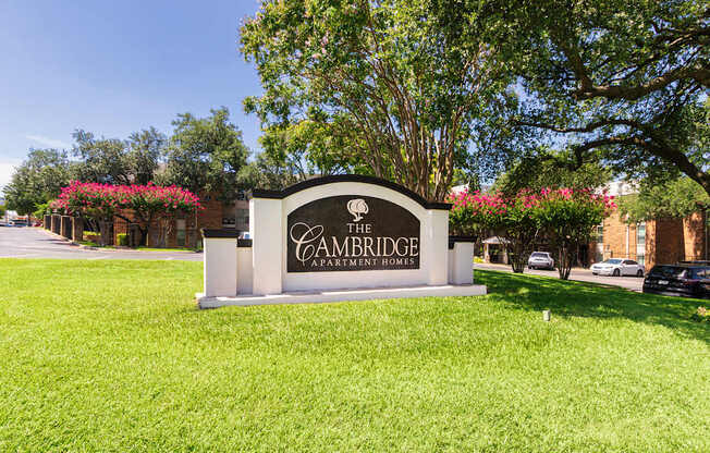 A sign for Cambridge Apartment Homes is in a grassy area in front of Cambridge Court Apartments Entryway in Lake Highlands, Dallas, TX.