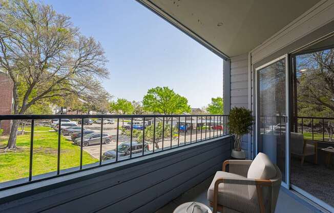 A balcony with a chair and a potted plant overlooking a parking lot.