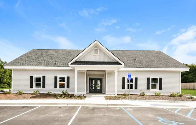 A small white building with a black door and windows, a sign on the door, and a parking lot in front.