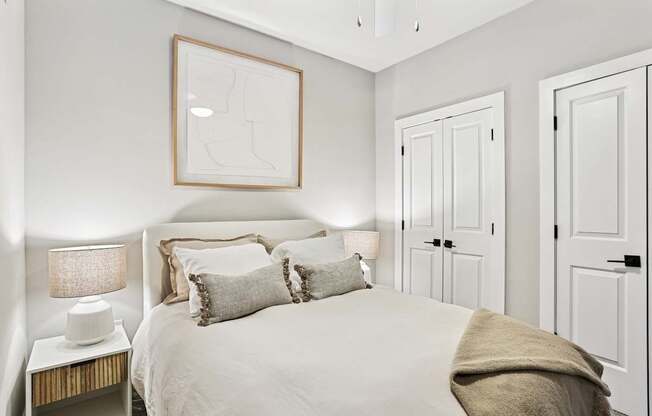 A bedroom with a bed, two lamps, and a picture on the wall.