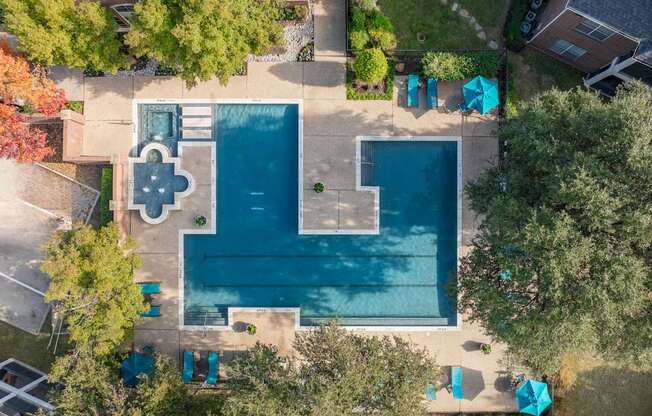 An aerial view of a swimming pool surrounded by trees and a small building.