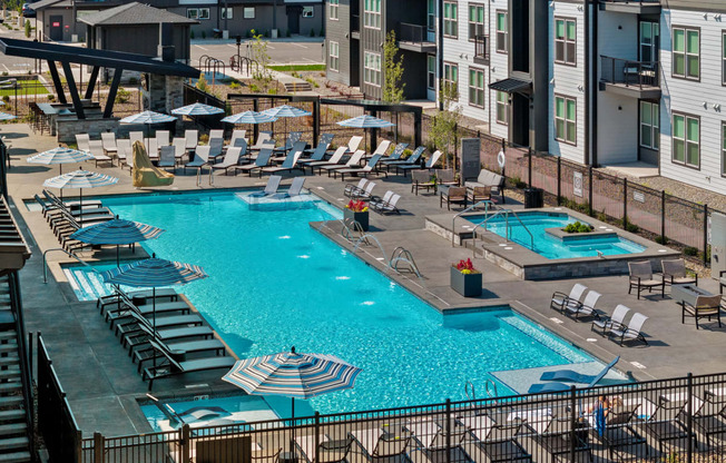 a swimming pool at an apartment complex with chairs and umbrellas