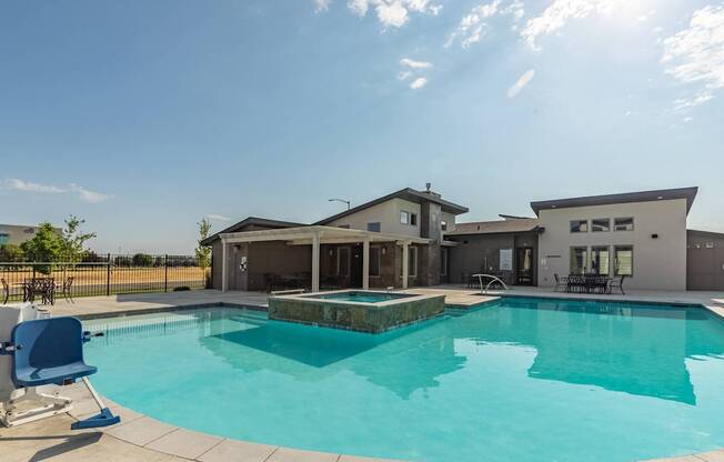 A swimming pool in front of a house with a sunny sky.