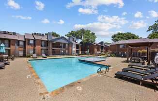 A swimming pool surrounded by sun loungers and apartment buildings.