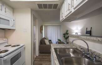 A kitchen with a white cabinets and appliances in a 515 square foot 1 bedroom, 1 bath apartment home at Canyon Creek Apartments in Dallas Midtown neighborhood of Dallas, TX.