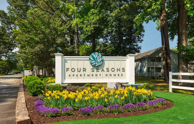 A sign for Four Seasons Apartment Homes is surrounded by flowers and greenery.