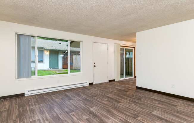 Pinewood Terrace Apartments | Living Room with large window, front door and view of patio sliding door in dining room.