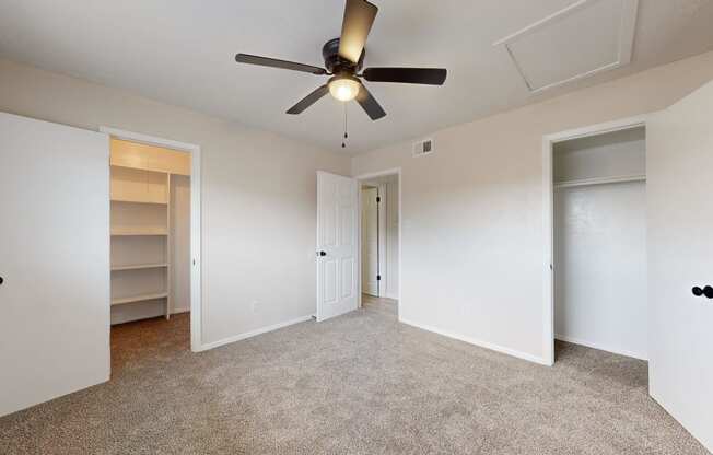 an empty bedroom with a ceiling fan and closet