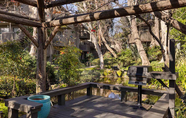 A wooden deck with a barbeque overlooking a lake.