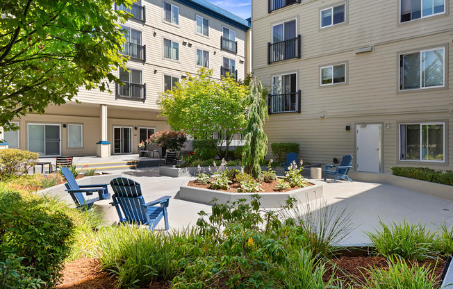 a courtyard with a large tree in the center and Adirondack chairs in front of the property building at Guinevere Apartment Homes, Seattle, 98103