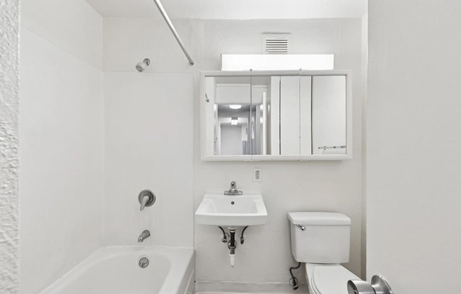 A white bathroom with a tub, sink, toilet and mirror.