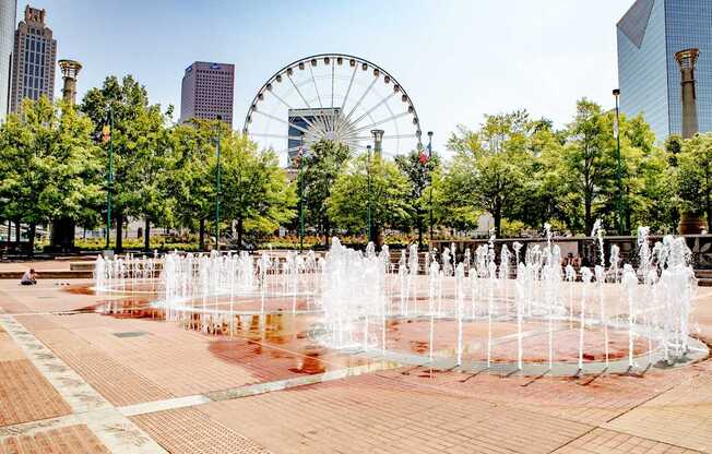 A fountain in the middle of a square with a Ferris wheel in the background.