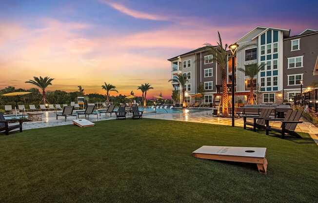 a swimming pool with lounge chairs and tables and a sunset in the background