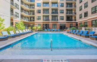 A large pool surrounded by lounge chairs and apartment buildings.