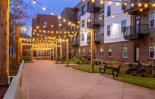A walkway with a bench and lights leading to a building.
