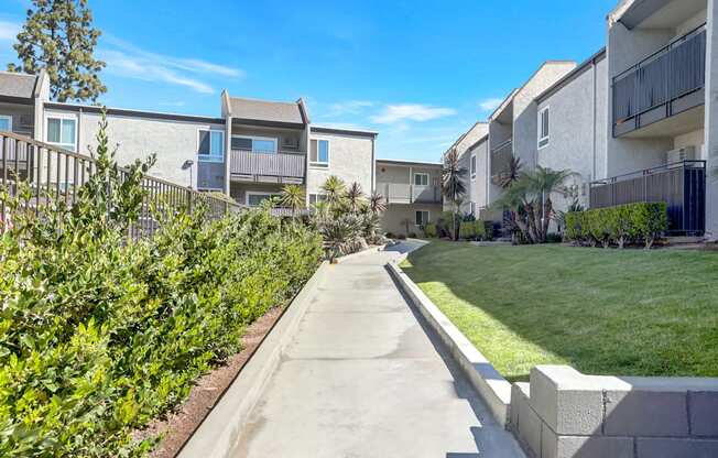 A concrete pathway leads through a well-manicured grassy area in front of apartment buildings.