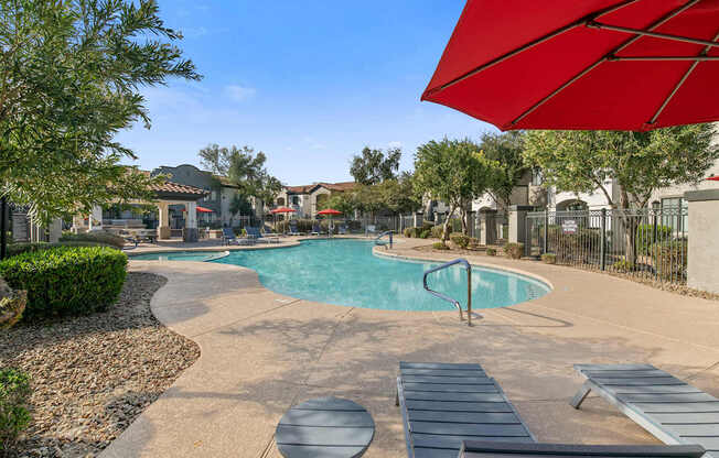 A pool surrounded by a concrete patio and a red umbrella.