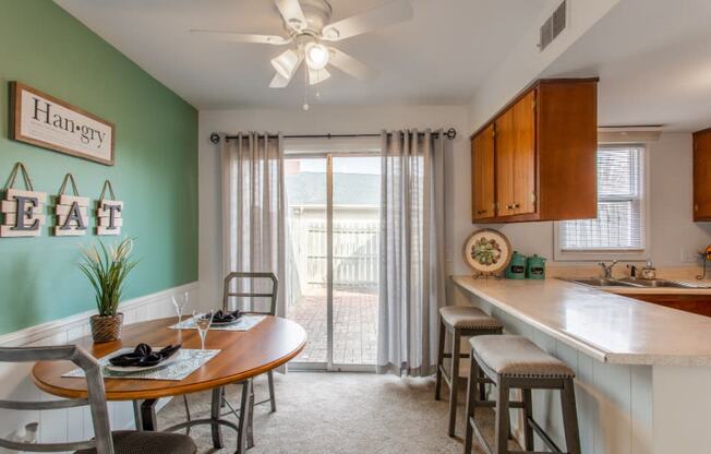 Model unit dining area with a table and chairs next to a kitchen with a sliding glass door