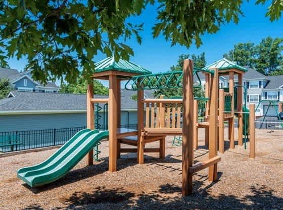 A playground with a green slide and wooden play structure.