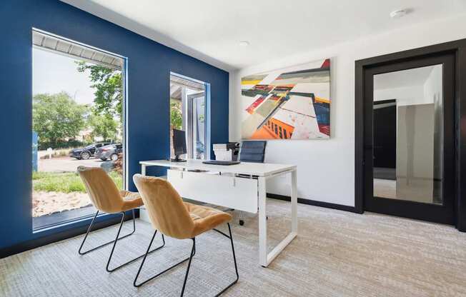 A room with a desk and chairs with a painting on the wall.