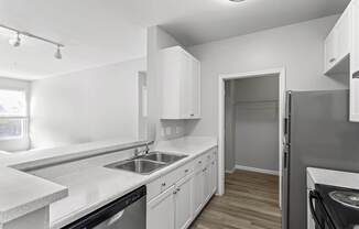 An updated kitchen at Ten05 West Trade Apartments, featuring stainless steel appliances like a dishwasher, refrigerator and sink. The flooring is brown luxury vinyl tile and the stove is black.