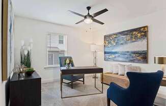 A blue chair sits in a room with a ceiling fan and a painting on the wall.