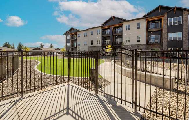 A black metal fence surrounds a playground area in front of apartment buildings.