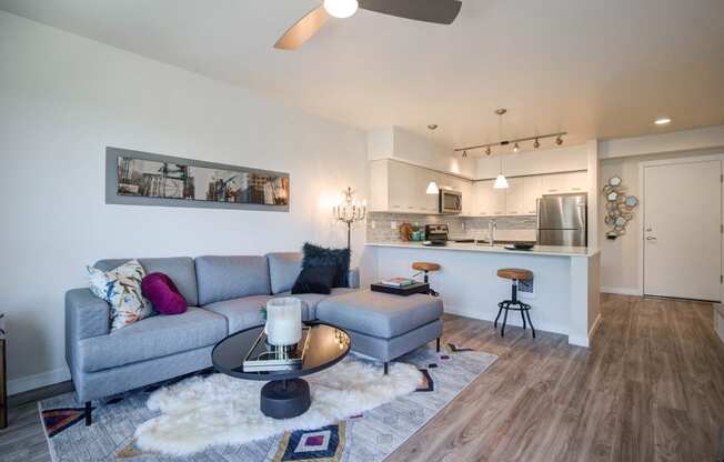 Living Room with Wood Inspired Floor, Gray Sofa, Barstools, Kitchen Countertop and Ceiling Fan/Light