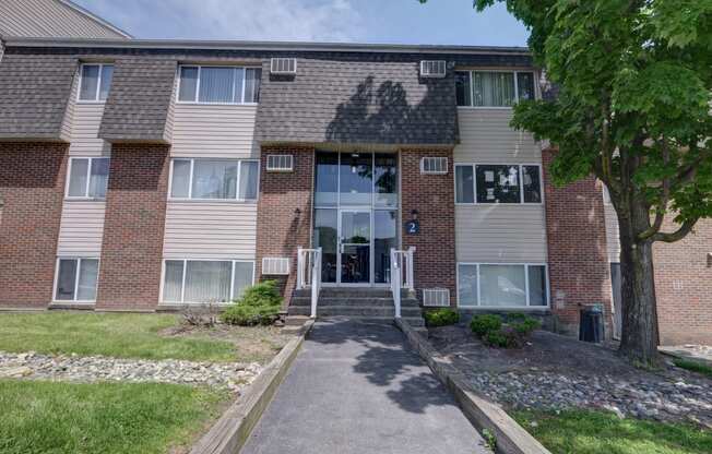 front view of a brick apartment building with a walkway and grass at Highland Club apartments, Watervliet, NY 12189