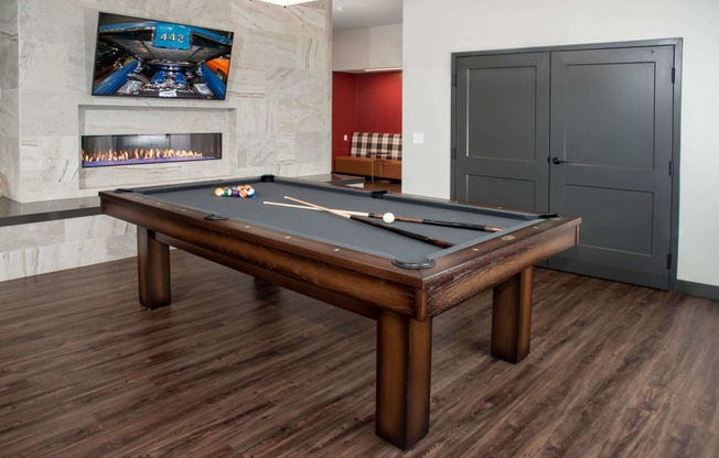 Pool table in community space across from fireplace and mounted TV.