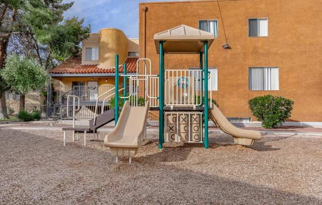A playground with a slide and a swing set in front of a building.