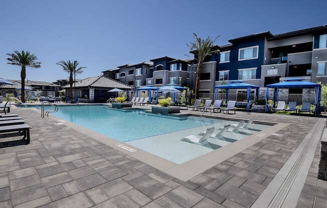 A swimming pool surrounded by a tiled patio and lounge chairs & private cabanas.