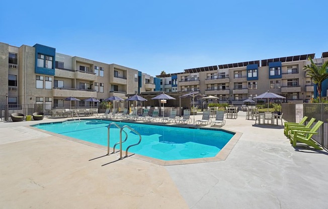 A swimming pool in a courtyard surrounded by chairs and umbrellas.