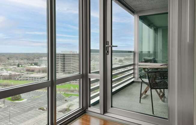 A balcony with a table and chairs overlooking a parking lot and buildings.