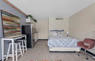 A bedroom with a bed, chair, and a fridge.